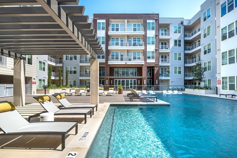 A large swimming pool with sun loungers and a building in the background.