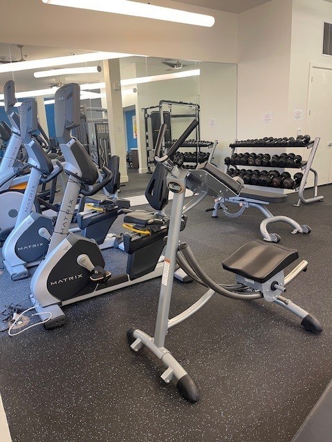 A gym with a variety of equipment including a stationary bike and a leg press machine.