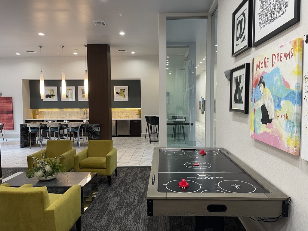 A shiny black air hockey table is in the middle of a room with yellow chairs.