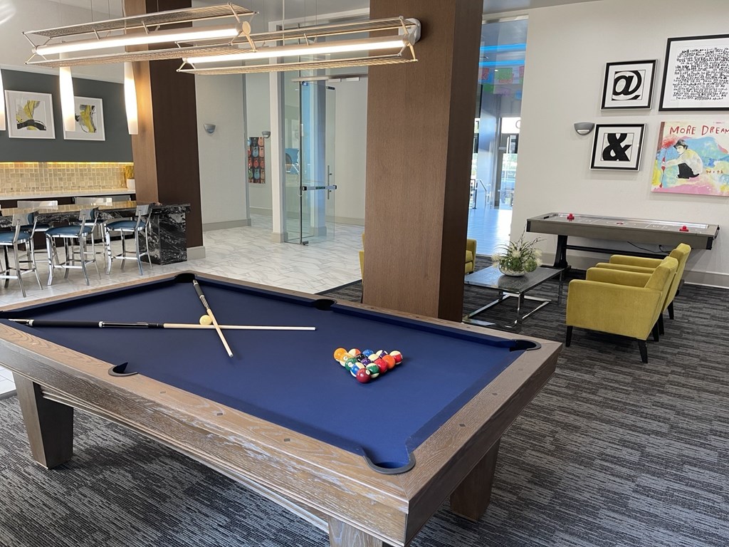 A pool table with a blue cloth and a yellow chair in the background.