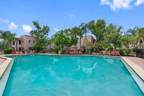 A swimming pool surrounded by red chairs and trees.