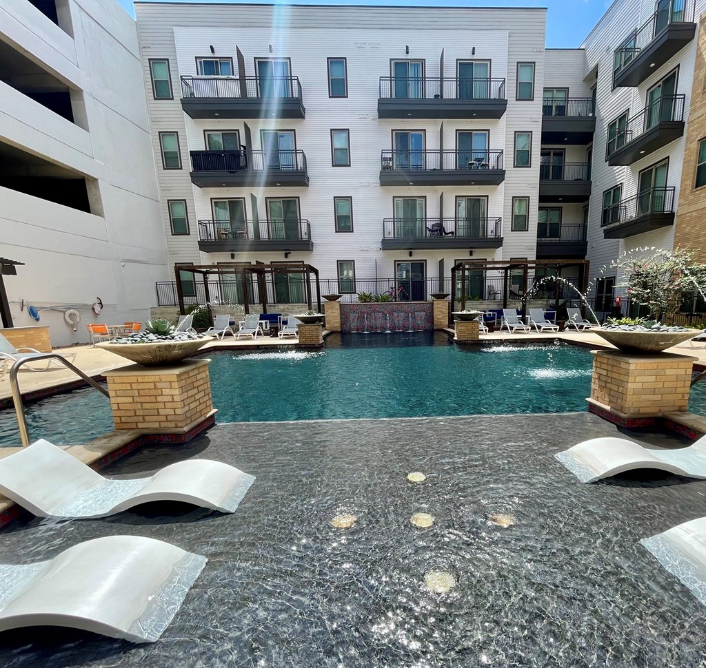 A pool surrounded by a concrete patio and lounge chairs.