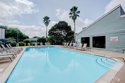 A large swimming pool with lounge chairs and a building in the background.