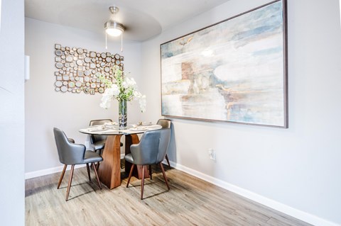A dining room with a table set for four and a large abstract painting on the wall.