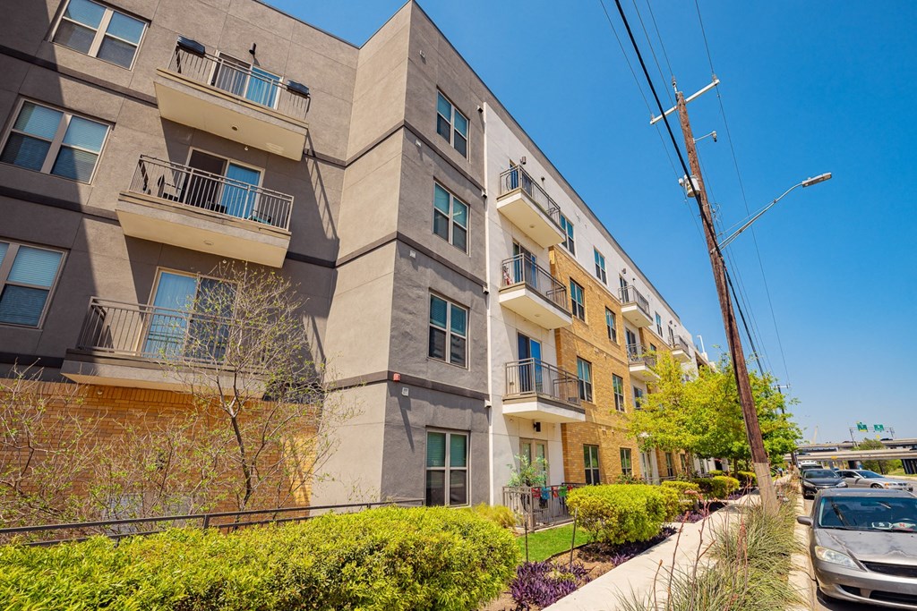 A row of modern apartment buildings with balconies and greenery in front.
