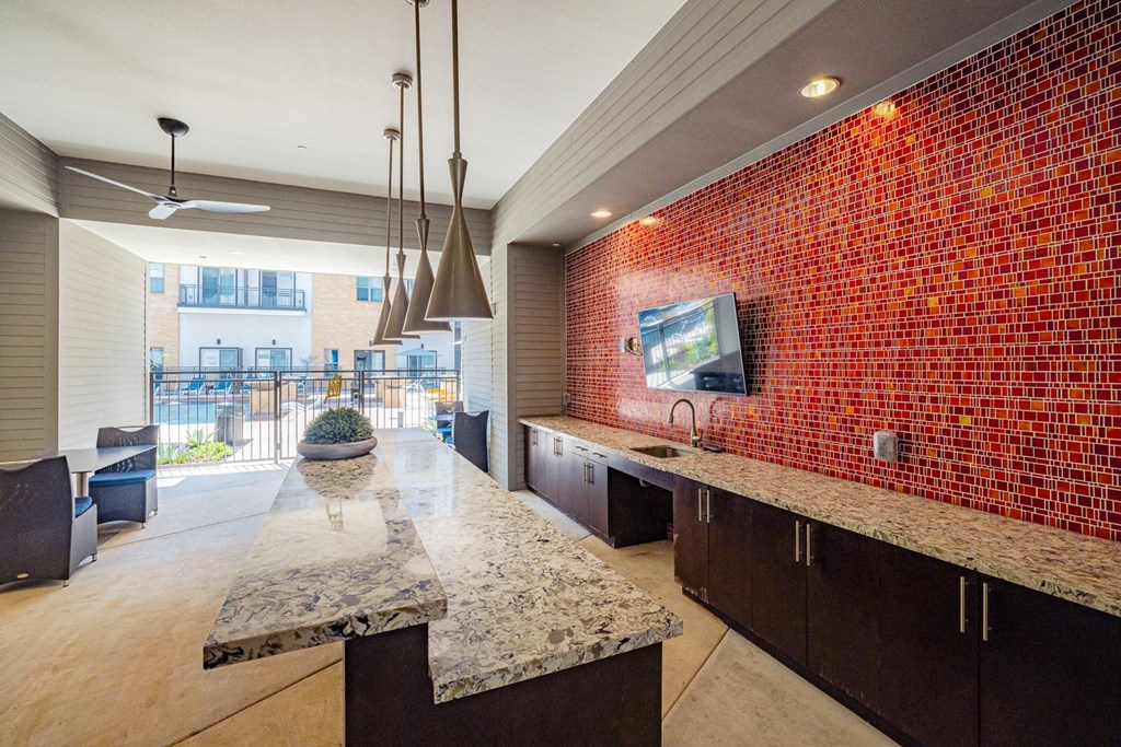 A modern kitchen with a red tiled wall and a marble countertop.