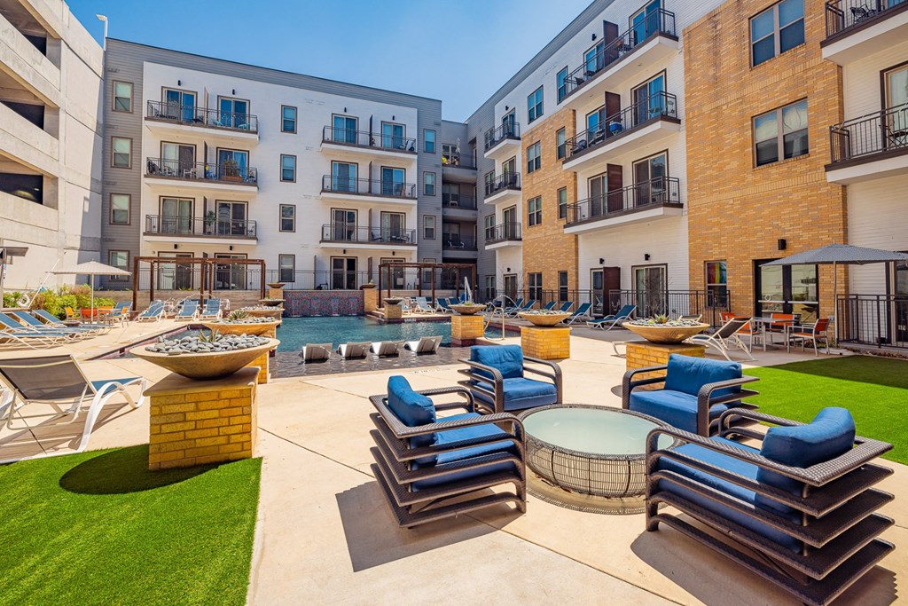 A sunny day at a modern apartment complex with a pool and lounge chairs.