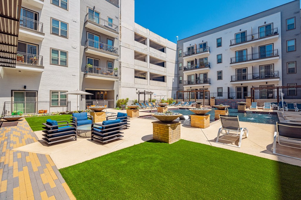 A sunny day at a modern apartment complex with a pool and lounge chairs.