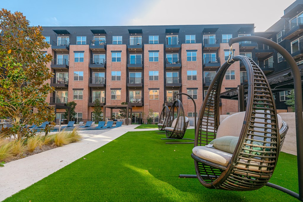 a courtyard with swing chairs and a lawn in front of an apartment building