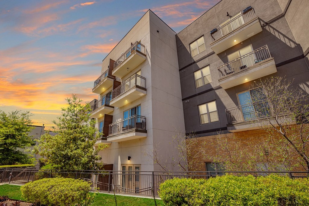 A modern apartment building with balconies and a sunset sky.
