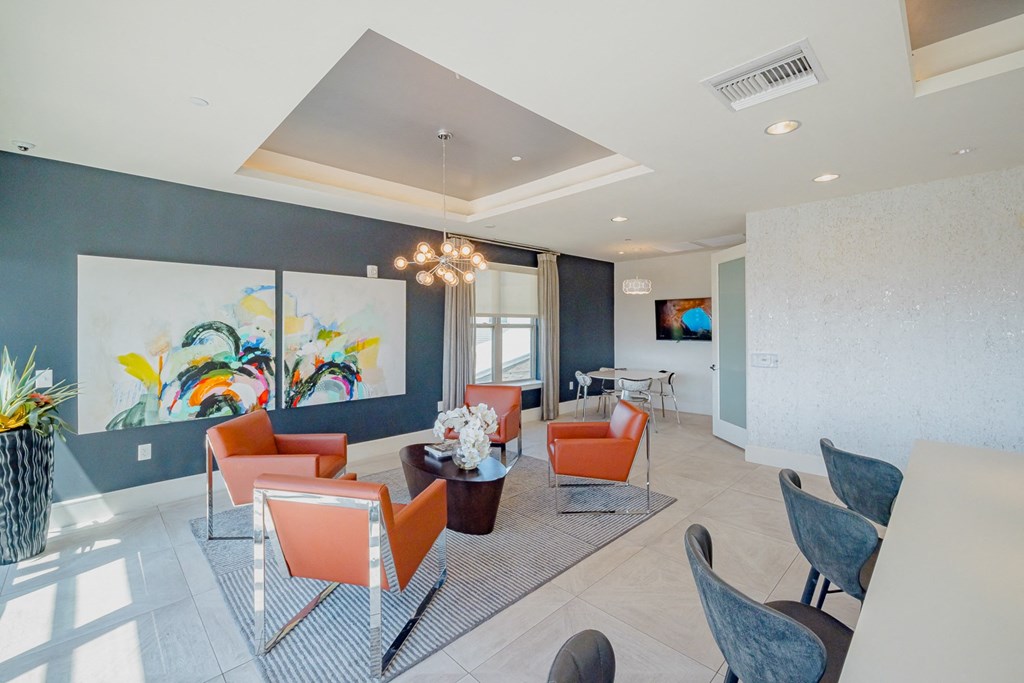 A modern living room with orange chairs and a large painting on the wall.