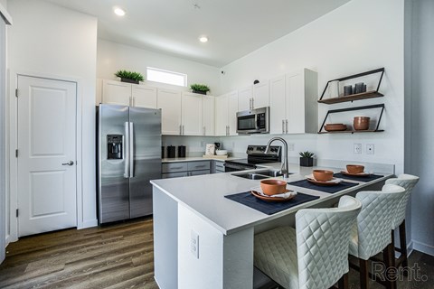 A kitchen with a white island and white chairs.