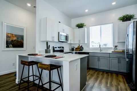 A kitchen with white cabinets and a white island with two stools.