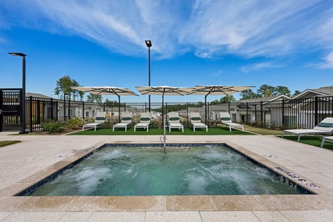 A pool area with a hot tub, chairs, and umbrellas.