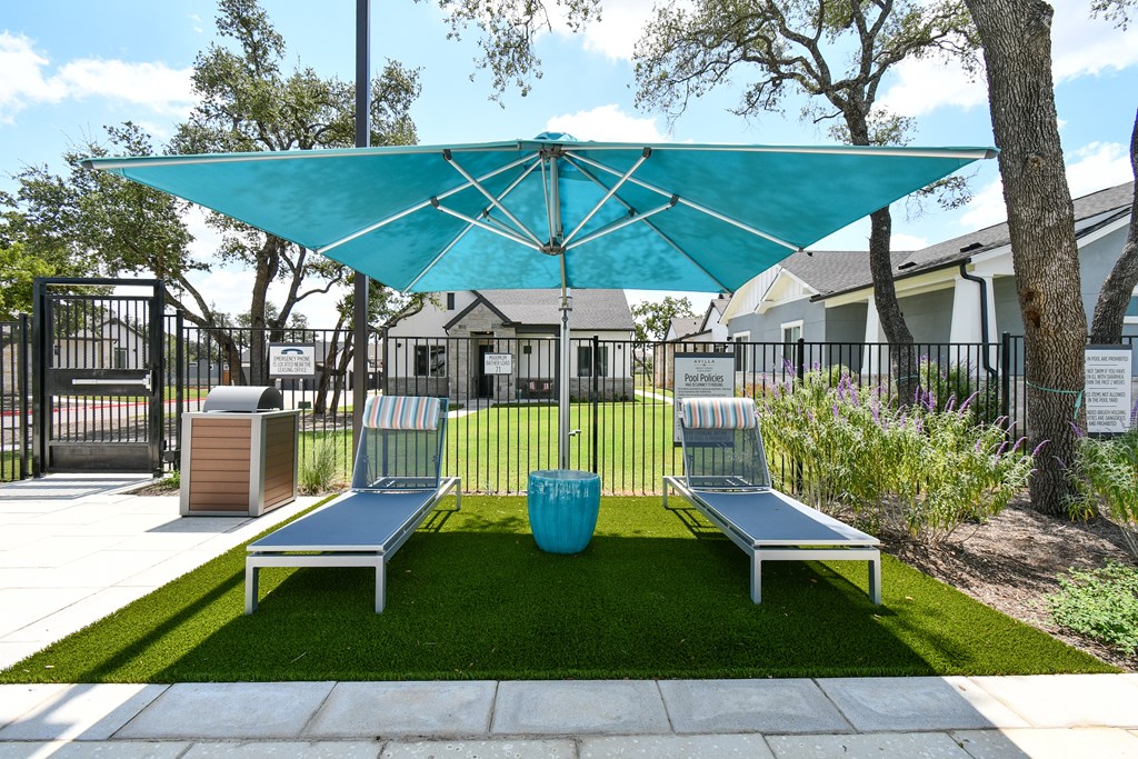 A blue umbrella shades a bench in a grassy area.