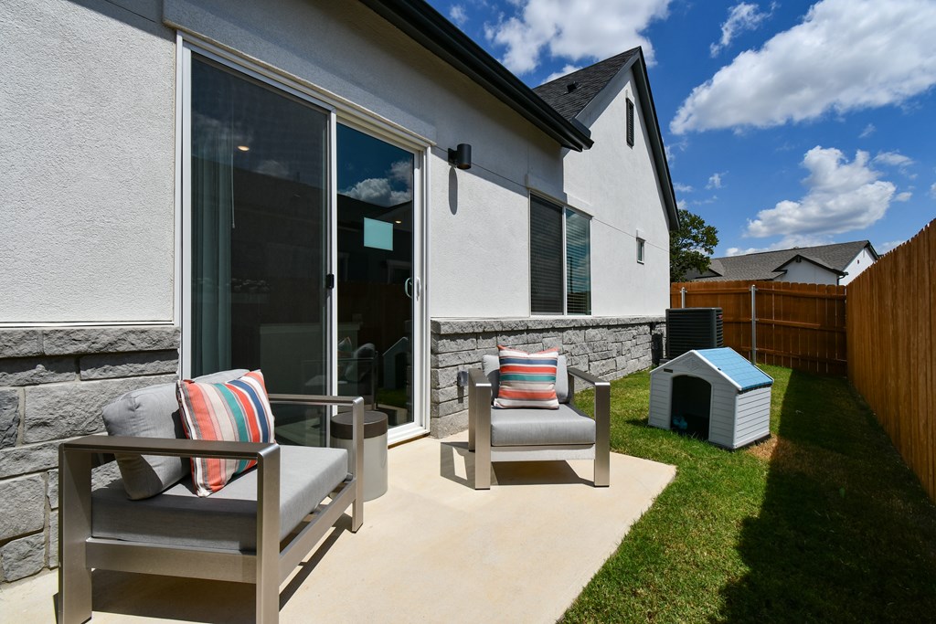 A patio with a grey couch and a striped pillow is in front of a house.