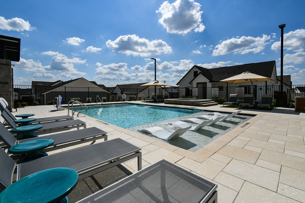 A pool area with sun loungers and a building in the background.