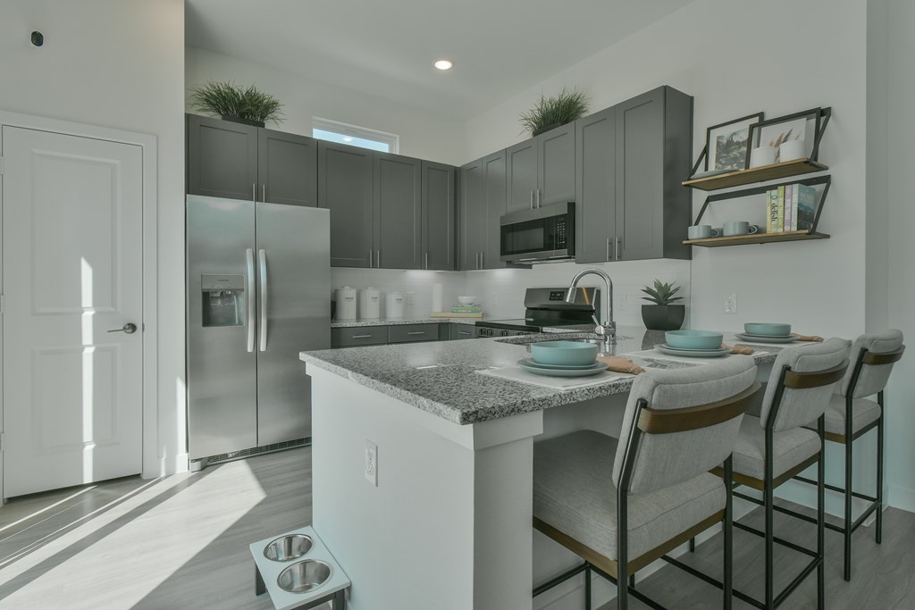 A kitchen with a refrigerator, microwave, and a counter with chairs.