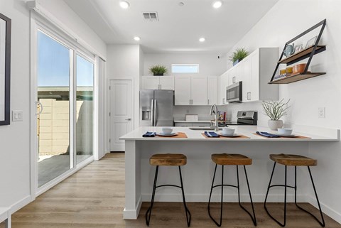 A kitchen with white cabinets and a white island with three bar stools.