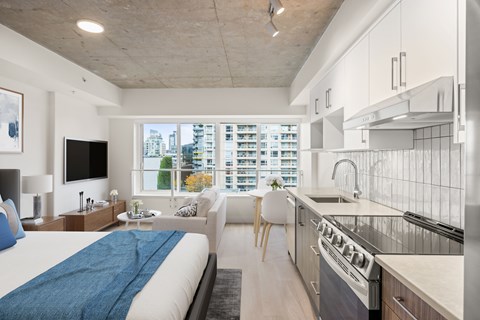 A modern living space with a large bed, a sofa, a flatscreen television, and a kitchen area.