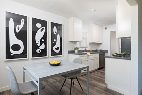 A modern kitchen with a table and chairs in front of a wall with three black and white paintings.