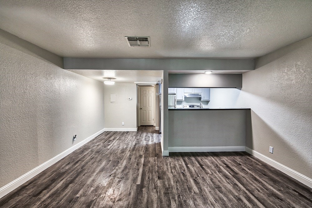 an empty living room with a kitchen in the background