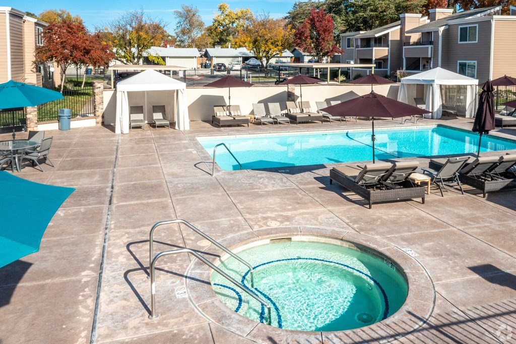 a swimming pool with chairs and umbrellas at an apartment complex