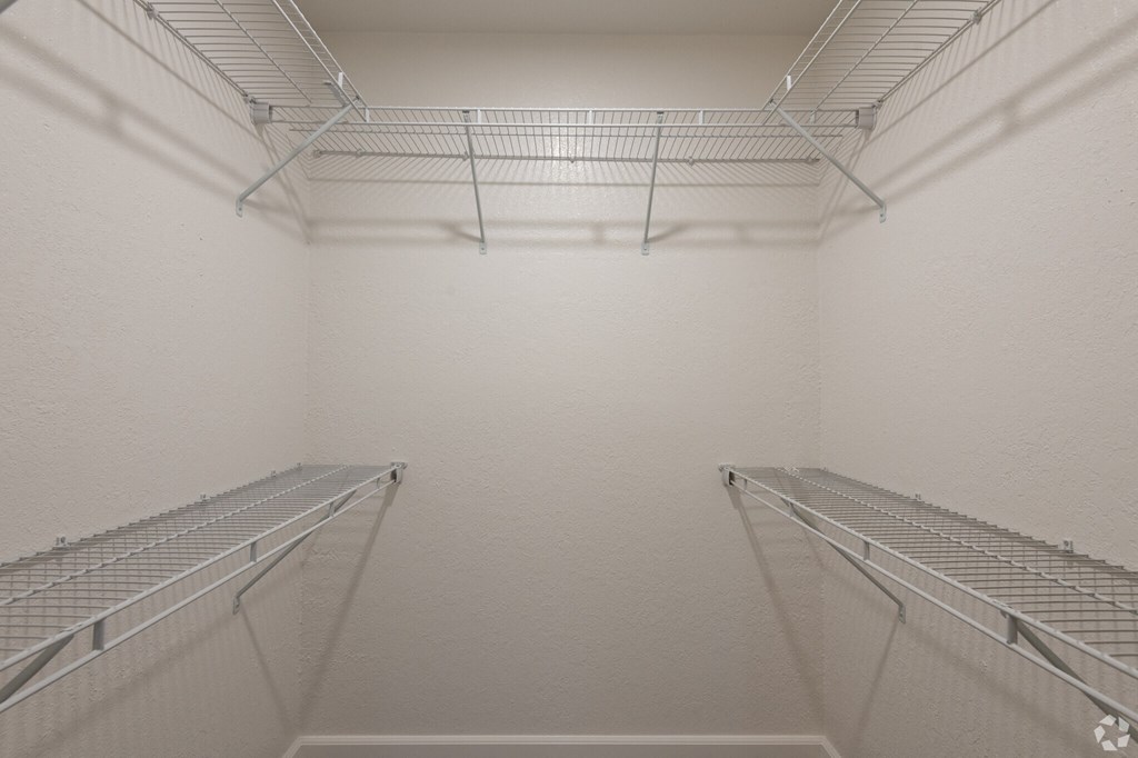 the walk in closet in a white room with two empty shelves