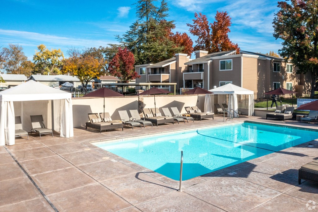a swimming pool with lounge chairs and umbrellas in front of an apartment building