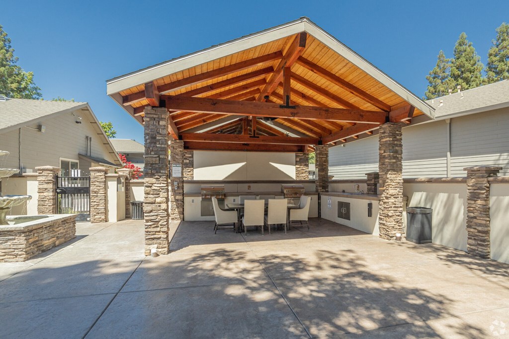 a large outdoor kitchen with stone pillars and a wooden roof