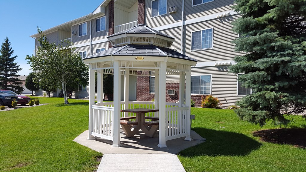 a gazebo with a picnic table in front of an apartment building
