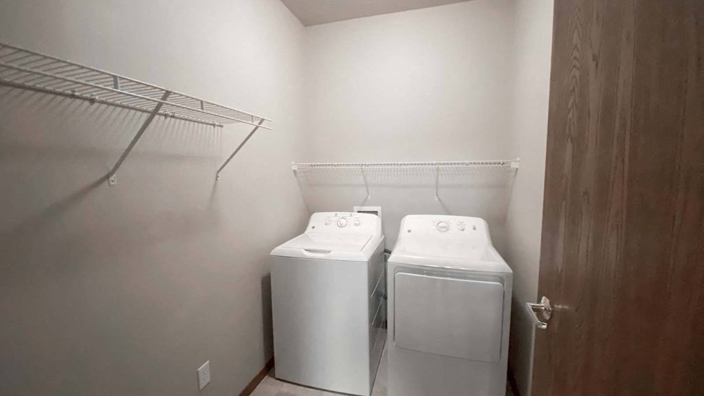In-unit washer and dryer with shelves in a large laundry room at Amber Crossing