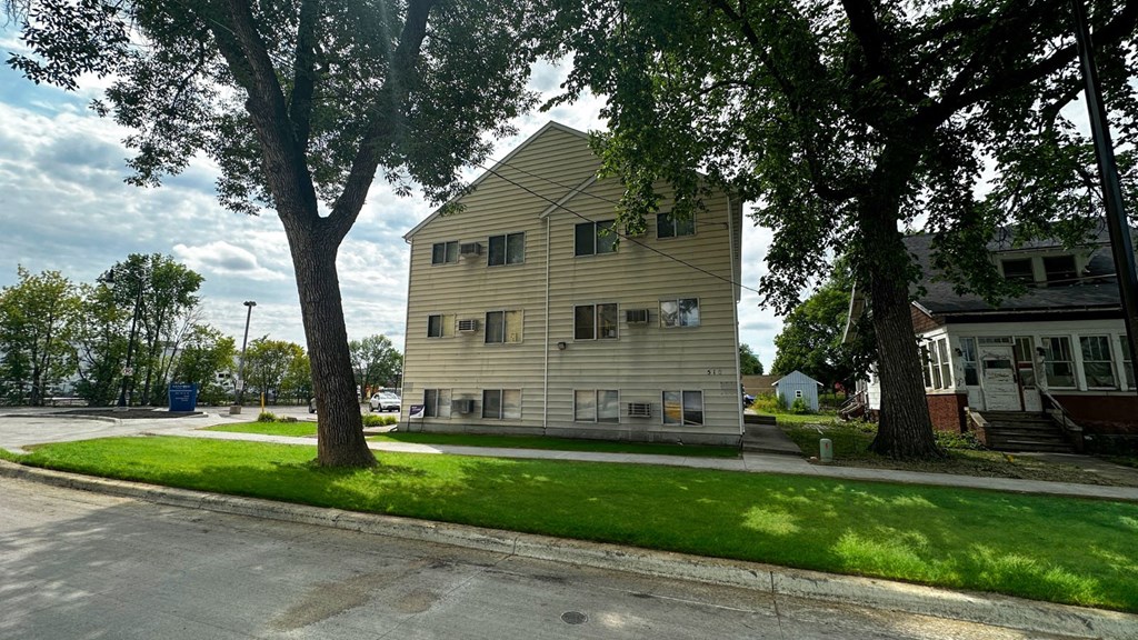 a yellow building with a triangular roof and two large trees in front of it