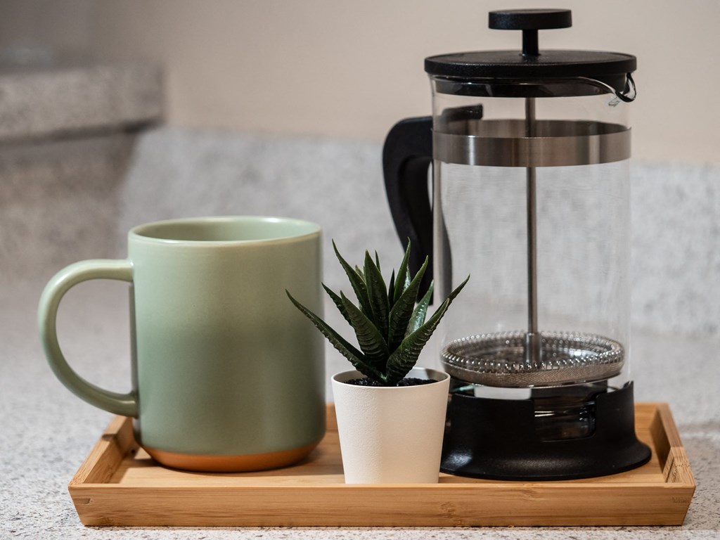 a coffee maker on a tray with a mug and a plant
