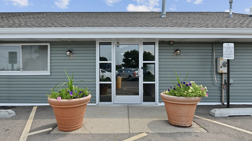 the front of a gray building with two large pots of flowersat Fox Run Apartments, St. Charles, IL