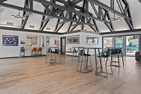 A room with a high ceiling and wooden floors has a bar area with stools.