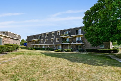a large brick apartment building with a green lawn and a tree at Aspen Ridge Apartments, West Chicago, 60185