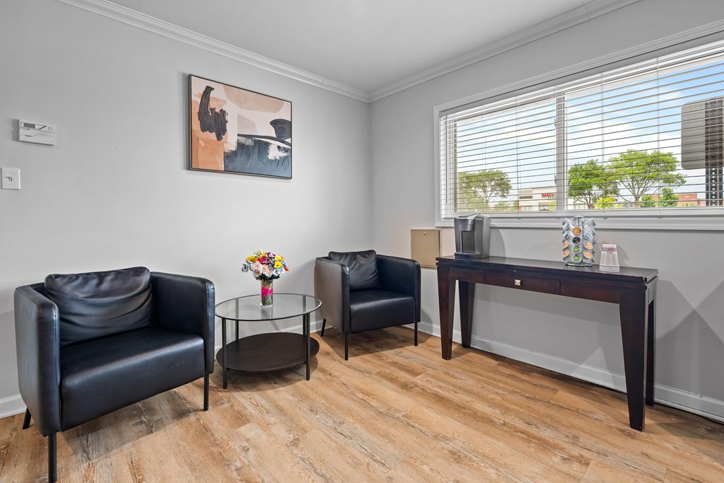 A living room with a black leather chair, a glass table, and a painting on the wall.