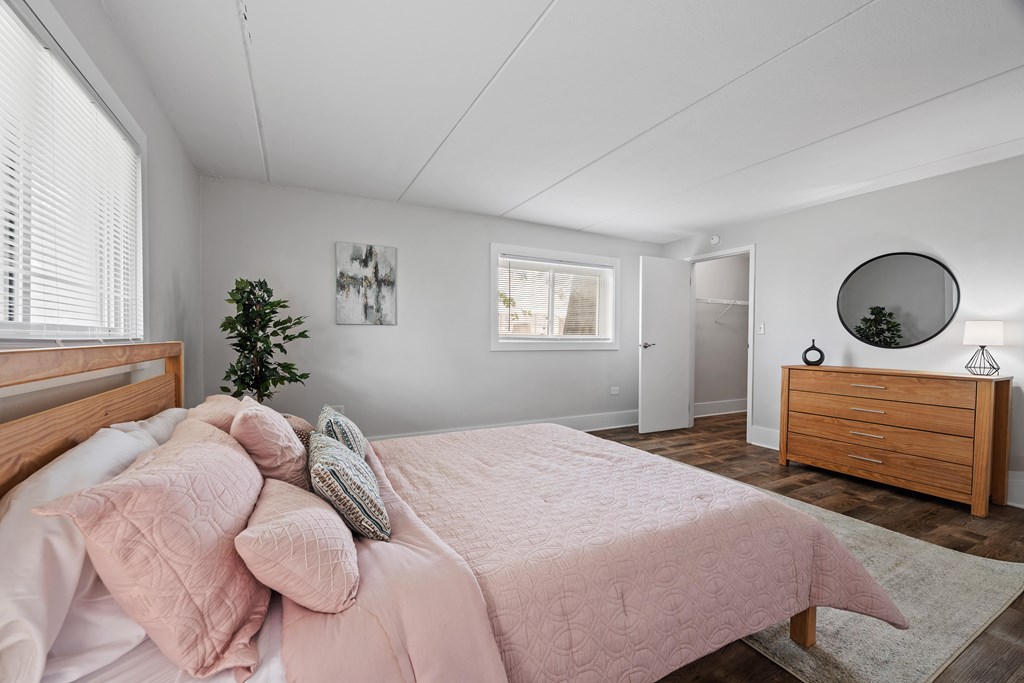 A bedroom with a bed, pillows, a plant, a mirror, and a dresser.