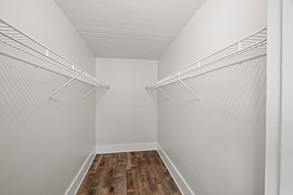 Empty walk in closet with white walls and wood floors.