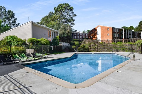 a swimming pool with green lounge chairs and a brick building in the background at Premier Apartments, Austell, GA, 30168