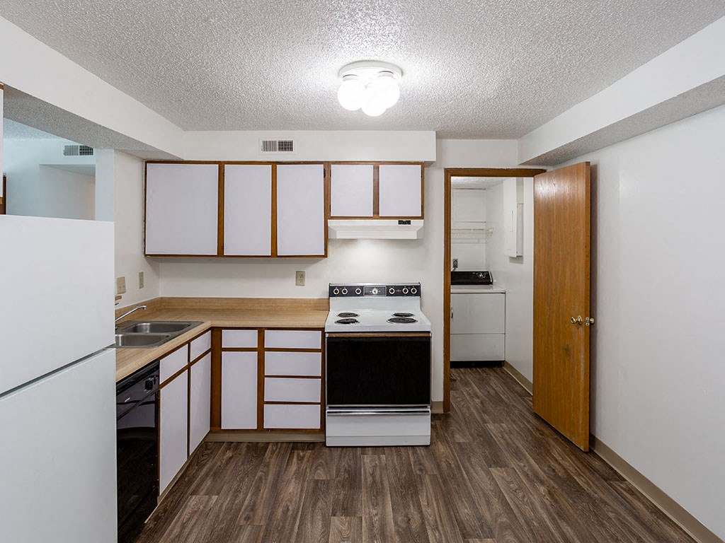 an empty kitchen with white appliances and wood floors