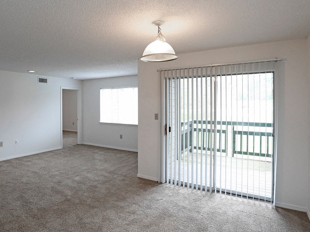 an empty living room with a sliding glass door to a balcony