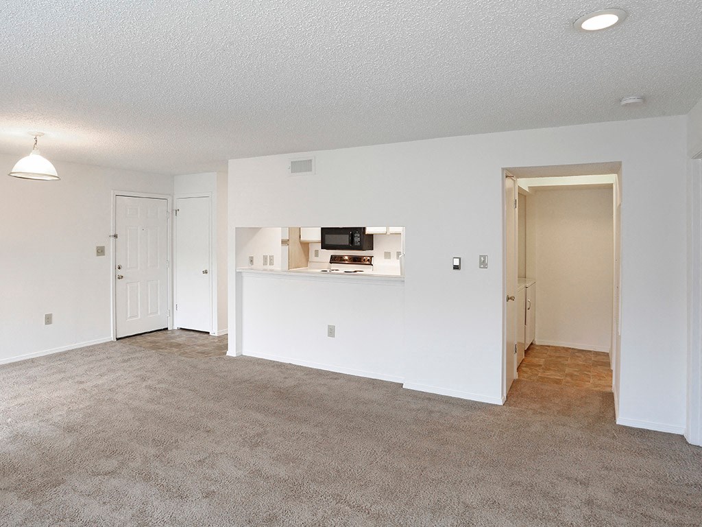 an empty living room with a kitchen in the background