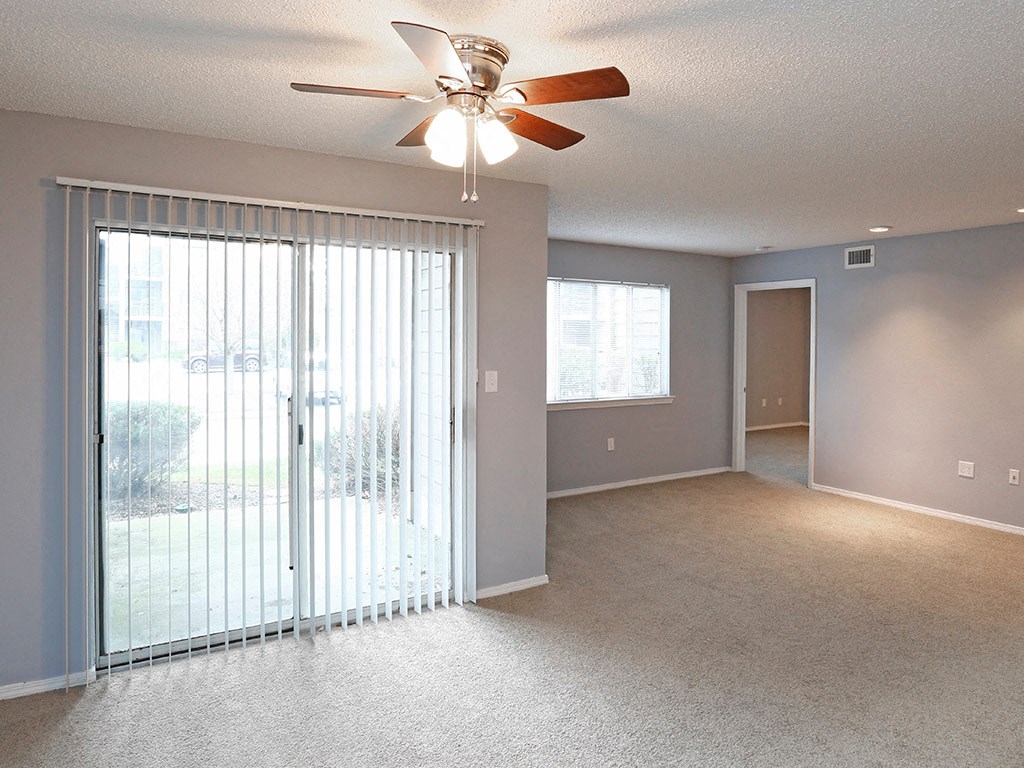 an empty living room with a large window and a ceiling fan