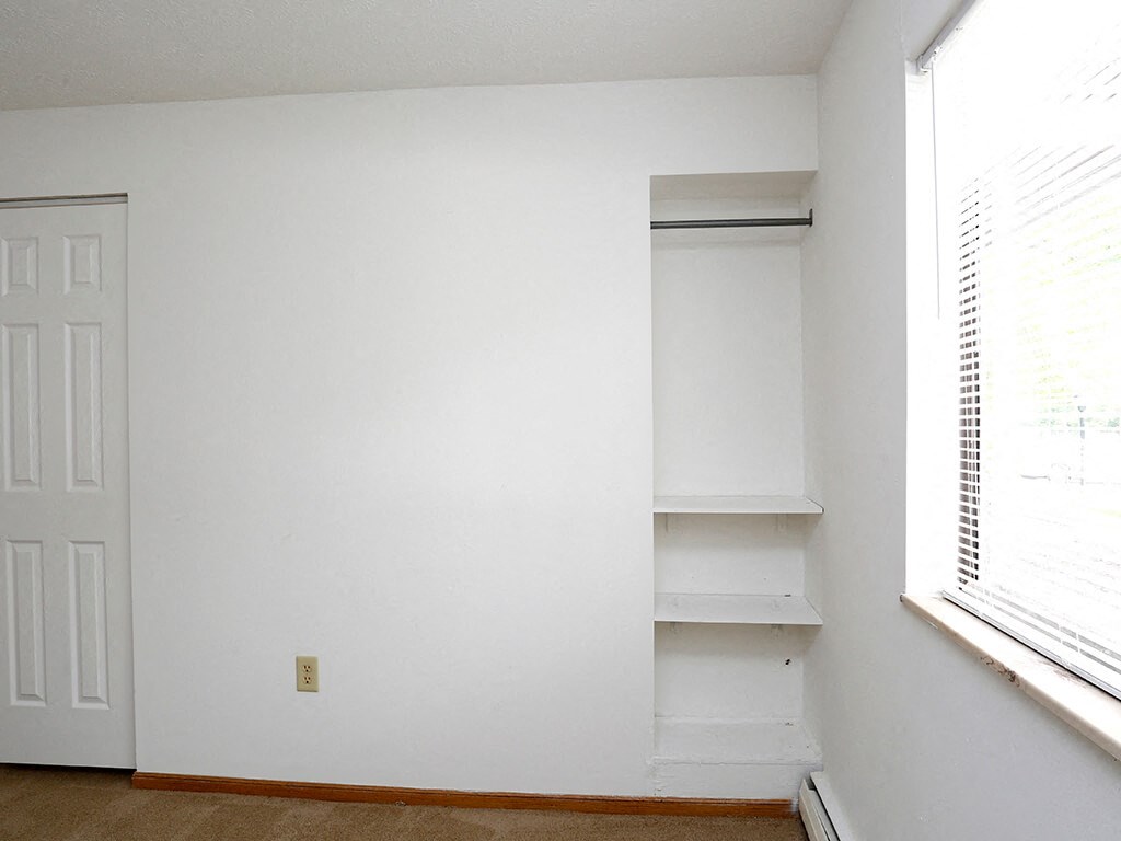an empty room with white walls and shelves and a window