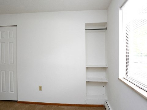 an empty room with white walls and shelves and a window