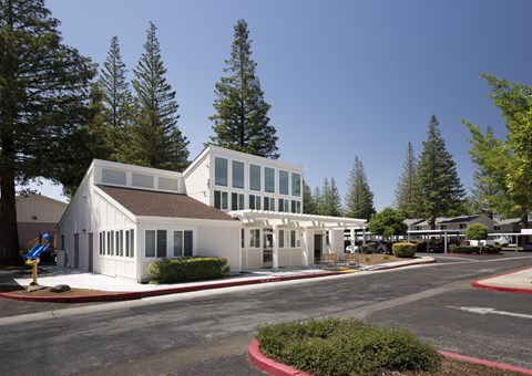 A white building with a brown roof is surrounded by trees.