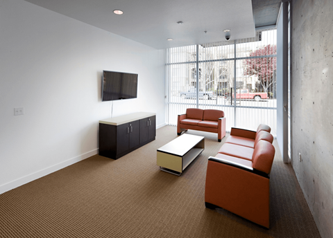 A living room with brown carpet and a television on the wall.