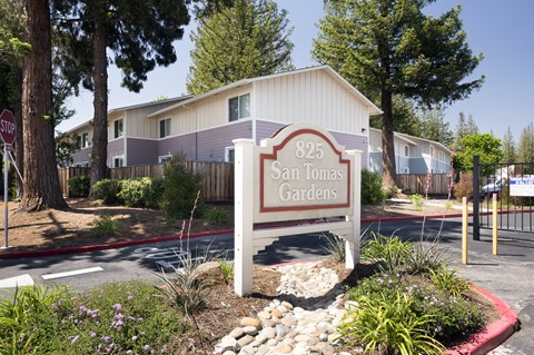 A sign for 825 San Tomas Gardens is in front of a building.